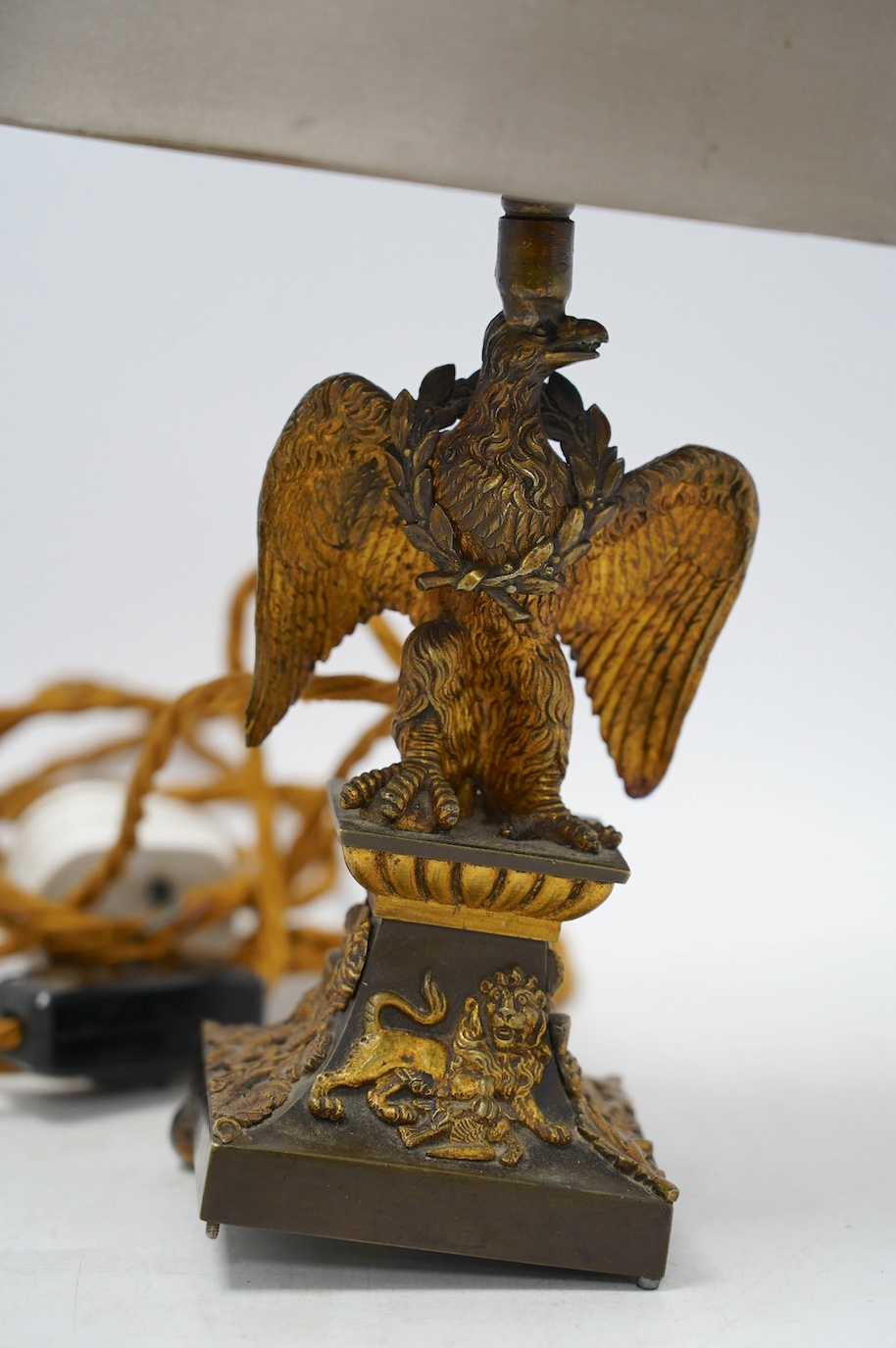 An ormolu table lamp in the form of an eagle with a laurel wreath around its neck, fitted with a grey shade, 39cm high overall. Condition poor to fair, three feet missing to lamp